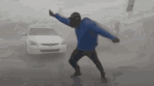 A person in a blue jacket gets blown sideways by strong wind.
